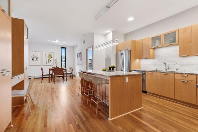 kitchen with a breakfast bar area, a center island, a sink, light wood-style flooring, and stainless steel appliances