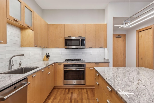kitchen featuring appliances with stainless steel finishes, light stone countertops, a sink, glass insert cabinets, and light wood-style flooring