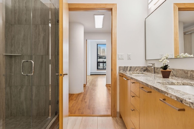 bathroom with double vanity, a sink, wood finished floors, and a shower stall