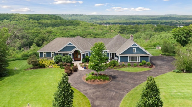 craftsman inspired home featuring a view of trees, curved driveway, a chimney, and stone siding