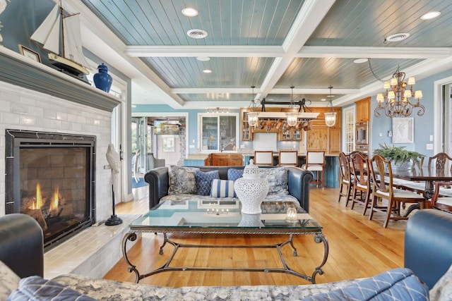 living area with a fireplace, beamed ceiling, a chandelier, coffered ceiling, and light wood-style flooring