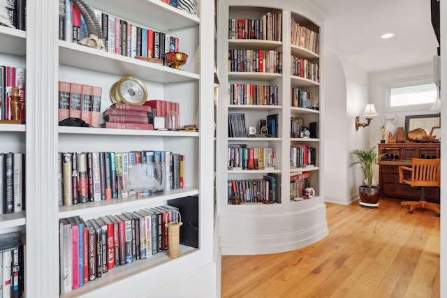sitting room with baseboards, wall of books, and wood finished floors