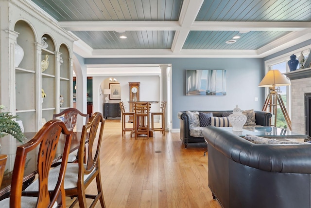 living room featuring a brick fireplace, beamed ceiling, wooden ceiling, and light wood finished floors