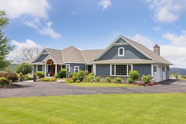 craftsman-style home with aphalt driveway, a chimney, a shingled roof, and a front lawn