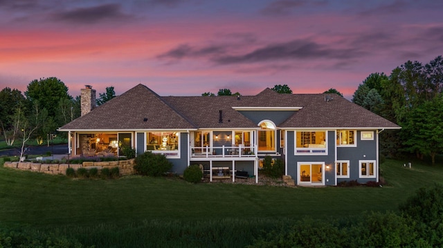 back of house at dusk with a yard, a chimney, and roof with shingles