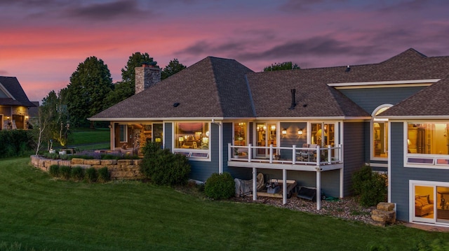 rear view of house featuring a lawn, a chimney, a shingled roof, and a deck