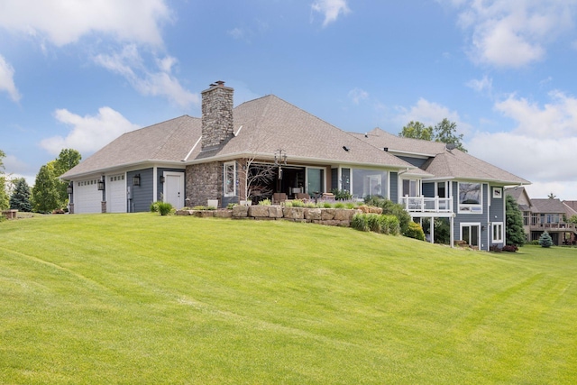 back of property with a lawn, an attached garage, a chimney, and a shingled roof