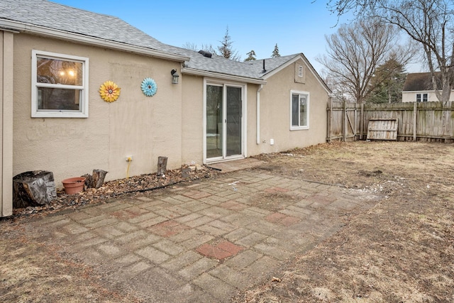 exterior space with roof with shingles, stucco siding, fence, and a patio