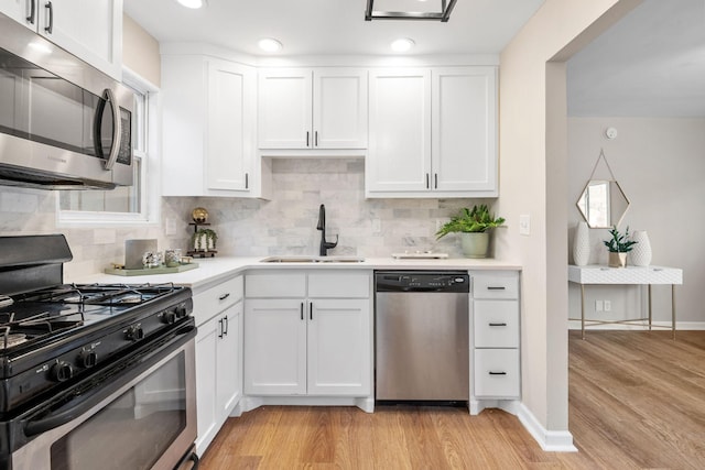 kitchen with white cabinetry, light countertops, stainless steel appliances, a sink, and light wood-style floors
