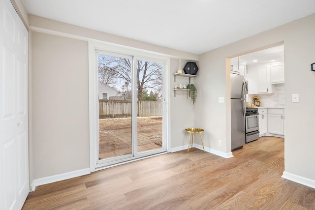 unfurnished dining area featuring baseboards and light wood finished floors