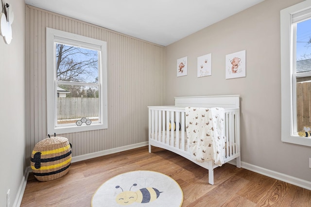 bedroom with multiple windows, wood finished floors, and a nursery area