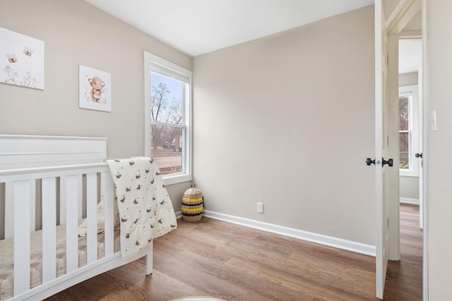 bedroom with baseboards, wood finished floors, and a crib