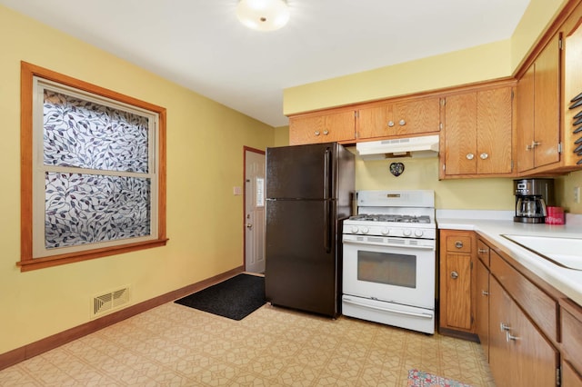 kitchen with light countertops, white gas range, freestanding refrigerator, under cabinet range hood, and visible vents