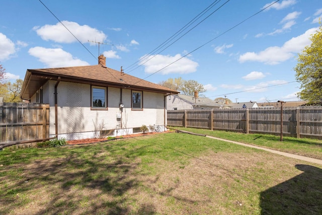 rear view of property featuring a lawn, a chimney, a fenced backyard, and roof with shingles