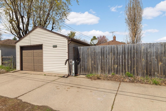 detached garage featuring concrete driveway and fence