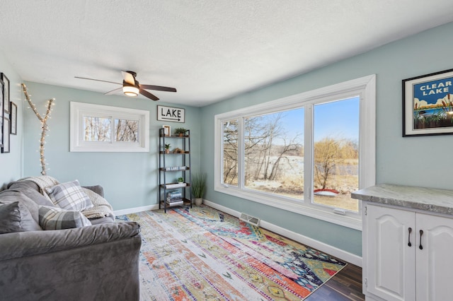 living area featuring baseboards, a ceiling fan, and a textured ceiling