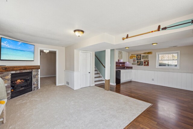unfurnished living room with dark wood finished floors, a stone fireplace, wainscoting, and stairs