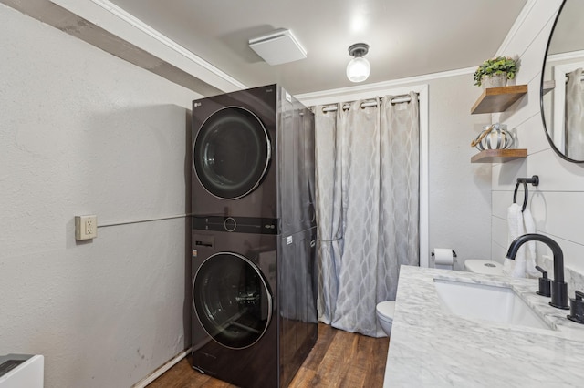 clothes washing area with a sink, laundry area, stacked washer / drying machine, and dark wood-style flooring