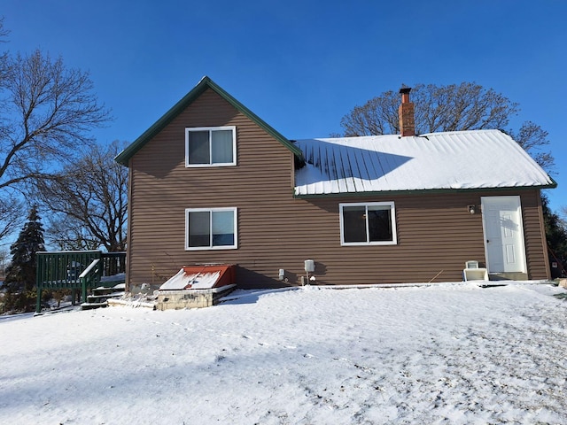 snow covered rear of property featuring a chimney, a deck, and metal roof