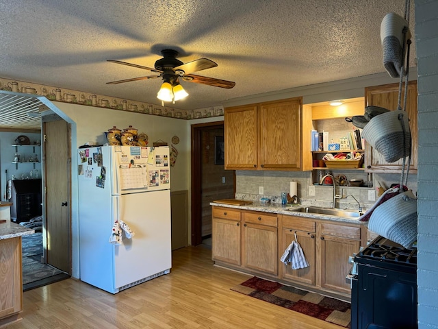 kitchen featuring light wood finished floors, black range with gas stovetop, a ceiling fan, a sink, and freestanding refrigerator