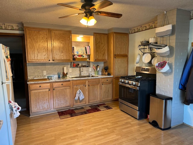kitchen featuring a sink, a ceiling fan, freestanding refrigerator, light wood-type flooring, and stainless steel range with gas stovetop