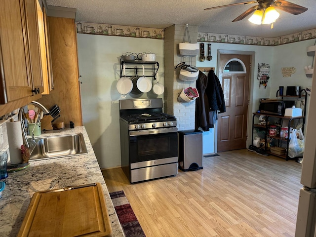 kitchen with a textured ceiling, a sink, stainless steel gas range, light wood-style floors, and ceiling fan