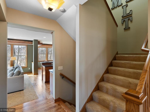 staircase featuring baseboards, wood finished floors, and lofted ceiling