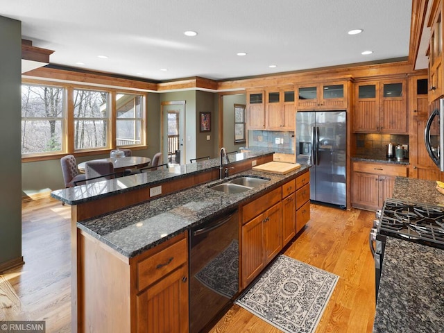 kitchen featuring a sink, stainless steel appliances, decorative backsplash, glass insert cabinets, and brown cabinetry