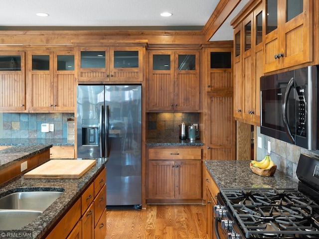 kitchen featuring tasteful backsplash, black range with gas cooktop, brown cabinetry, and stainless steel fridge with ice dispenser