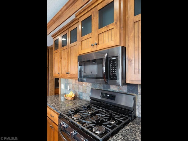 kitchen with appliances with stainless steel finishes, dark stone counters, decorative backsplash, and glass insert cabinets