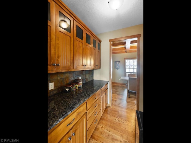 kitchen featuring glass insert cabinets, brown cabinets, decorative backsplash, and light wood-type flooring