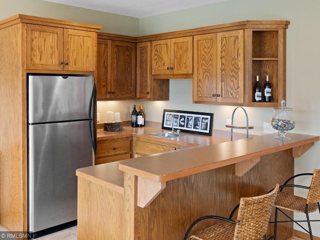 kitchen with a kitchen breakfast bar, open shelves, light countertops, freestanding refrigerator, and a peninsula
