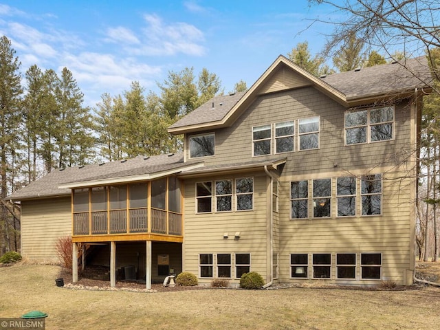 rear view of house with a yard, central AC unit, a shingled roof, and a sunroom