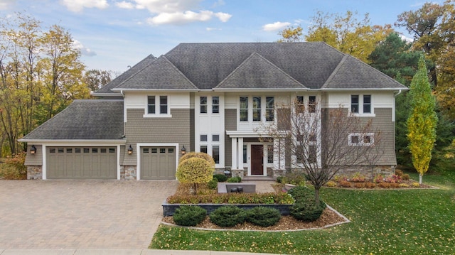 view of front of house featuring roof with shingles, driveway, stone siding, an attached garage, and a front lawn