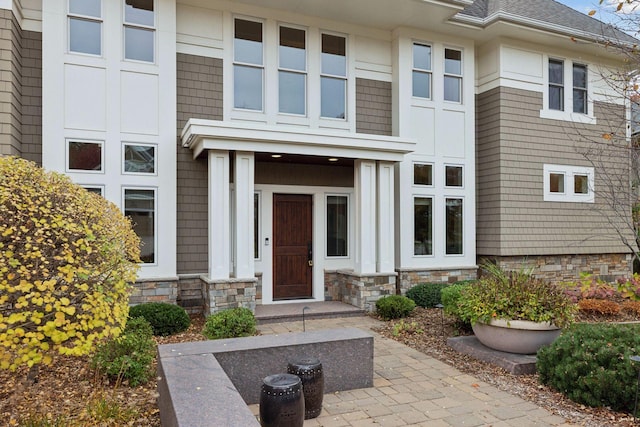 view of exterior entry with roof with shingles and stone siding