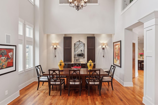 dining room featuring a chandelier, light wood-type flooring, a high ceiling, and a healthy amount of sunlight