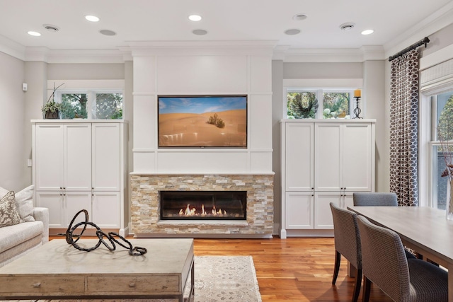 living area with ornamental molding, a stone fireplace, light wood finished floors, and recessed lighting