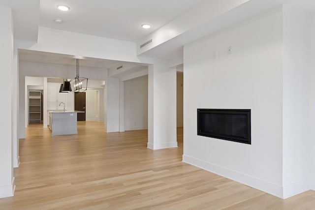 222 Ferndale Rd S Unit 207, Wayzata, MN 55391 - unfurnished living room with light wood-style flooring, a chandelier, and a glass covered fireplace