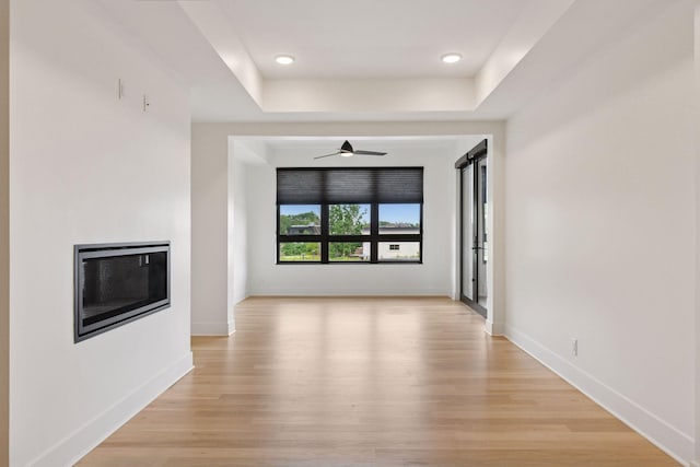 222 Ferndale Rd S Unit 207, Wayzata, MN 55391 - unfurnished living room featuring ceiling fan, light wood-type flooring, a glass covered fireplace, a tray ceiling, and recessed lighting