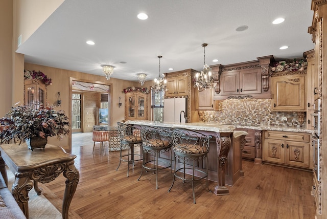 kitchen featuring light wood-style floors, an island with sink, a kitchen bar, tasteful backsplash, and recessed lighting
