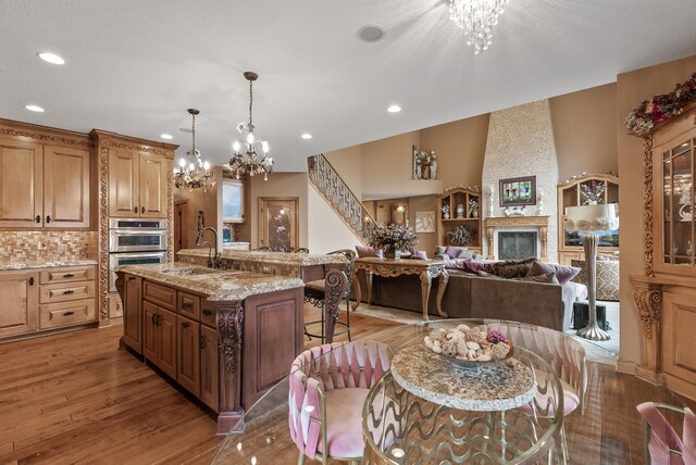 kitchen with a chandelier, stainless steel double oven, a breakfast bar area, light wood finished floors, and a sink