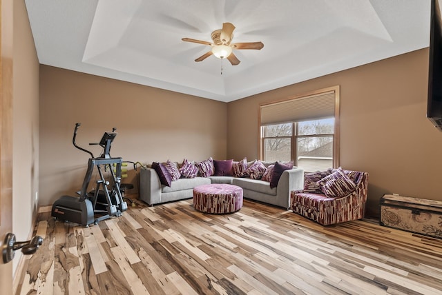 living area featuring a raised ceiling, a ceiling fan, and light wood-style flooring
