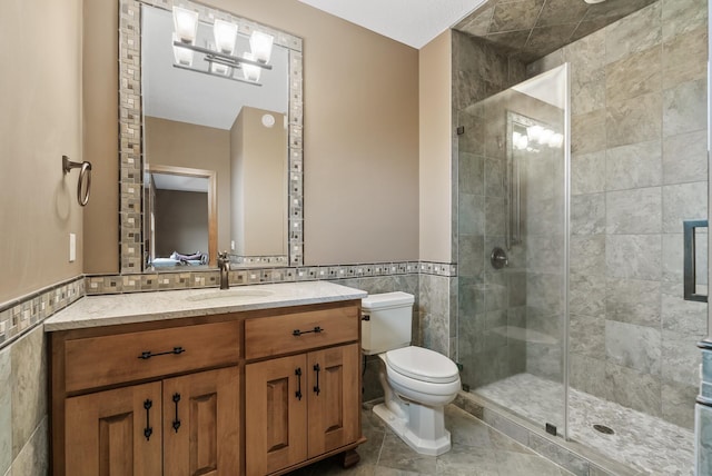 full bathroom featuring vanity, a wainscoted wall, toilet, a shower stall, and tile walls