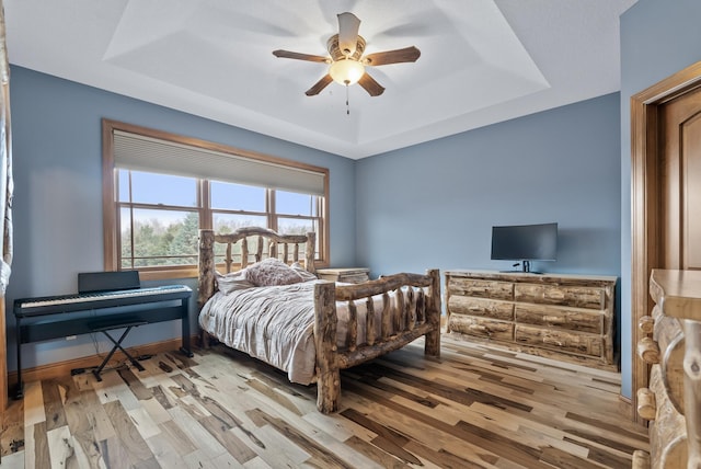 bedroom with a tray ceiling, wood finished floors, ceiling fan, and baseboards
