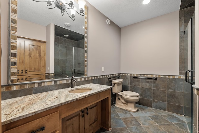 full bathroom featuring a stall shower, a textured ceiling, toilet, wainscoting, and tile walls