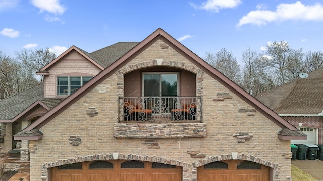 view of side of property featuring brick siding, an attached garage, a shingled roof, and a balcony