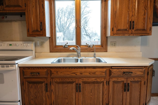 kitchen with white electric range oven, light countertops, brown cabinetry, and a sink
