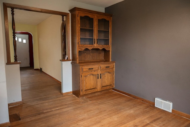 hall featuring visible vents, light wood-style flooring, arched walkways, and baseboards