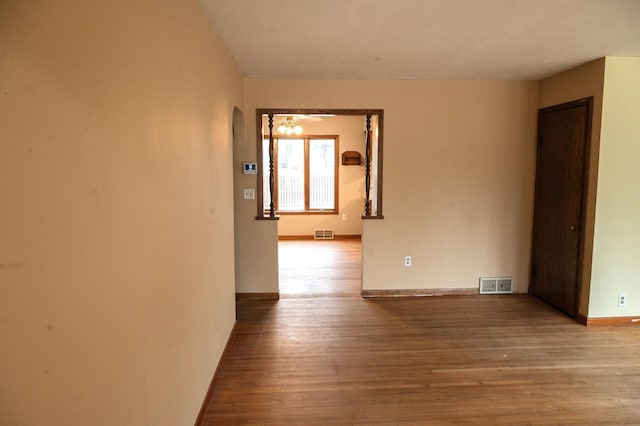 spare room featuring a chandelier, arched walkways, visible vents, and wood finished floors