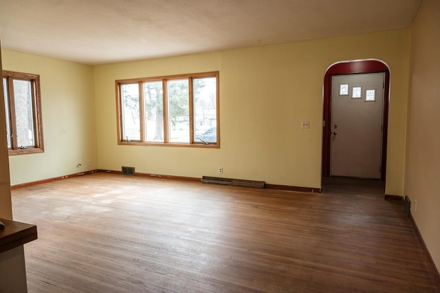 unfurnished living room with visible vents, baseboards, arched walkways, a baseboard radiator, and wood finished floors